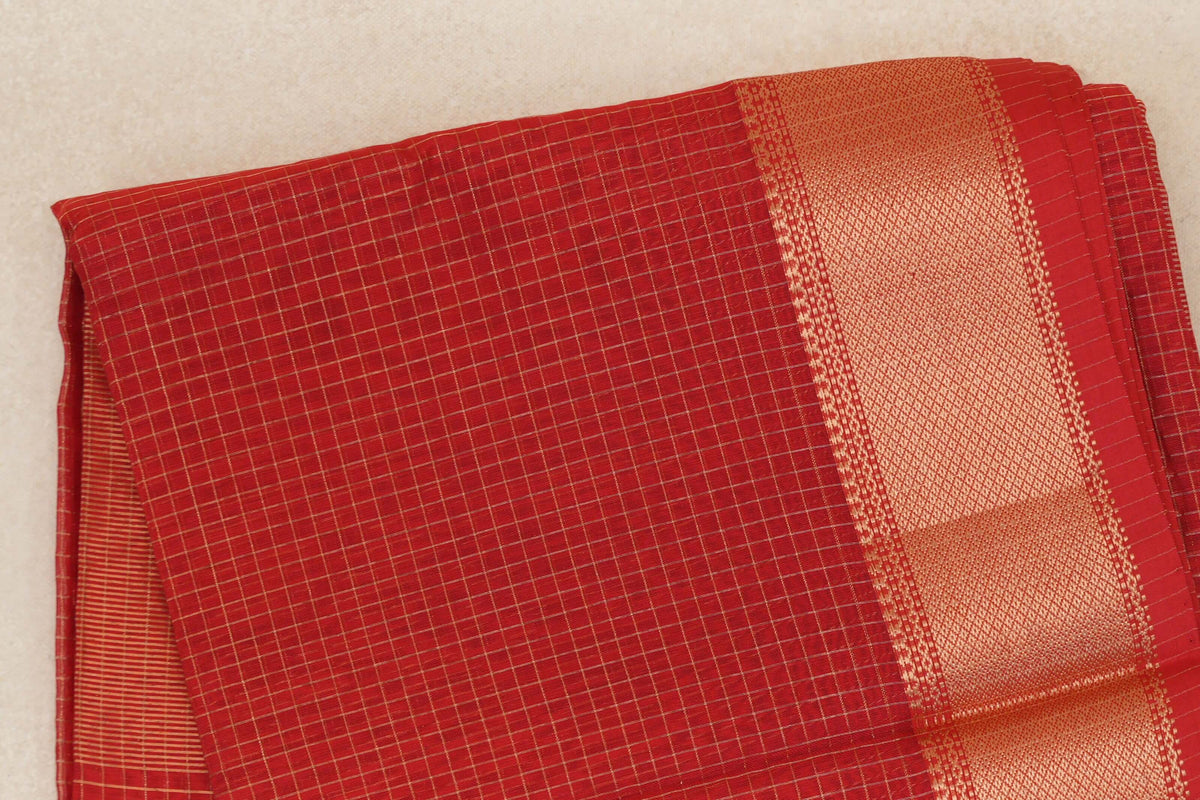 Folded tomato red Maheshwari silk cotton saree with a fine gold check pattern and a wide, textured gold zari border edged in red.