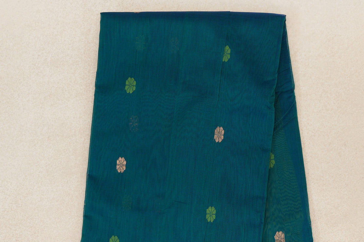 Folded teal blue Maheshwari silk cotton saree showing scattered small leaf green and pale gold floral motifs across the body.