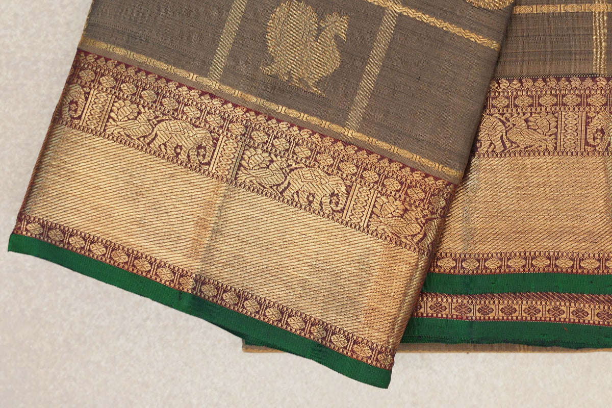 Folded olive green Kanjivaram silk saree showing a gold motif and a deep maroon border with gold elephant designs and bottle green selvedge.