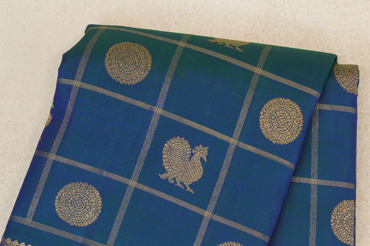Folded peacock blue Kanjivaram silk saree with fine gold checks, circular medallions and peacock motifs.