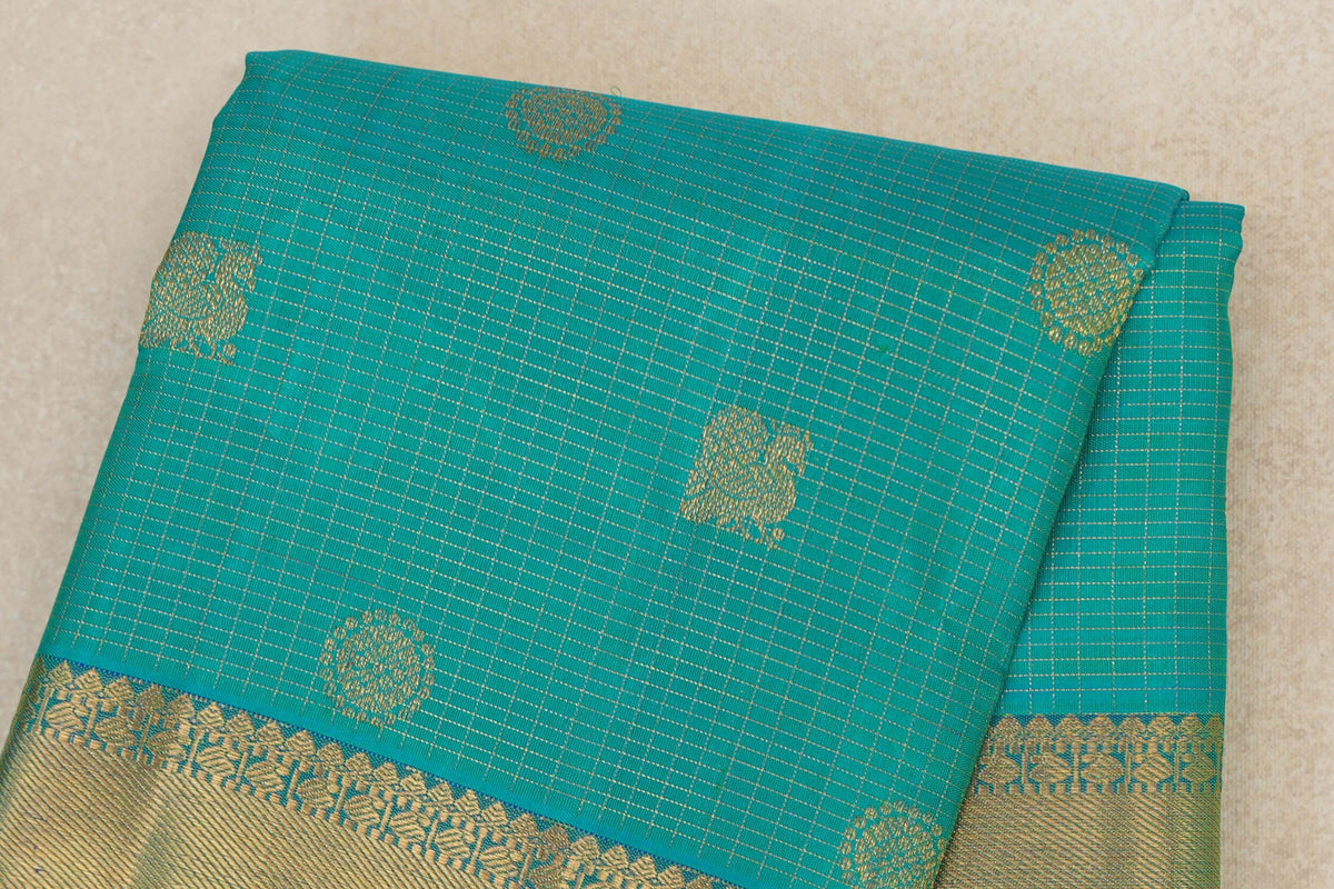 Folded aqua green Kanjivaram silk saree with fine zari checks, scattered gold motifs and a patterned gold border.