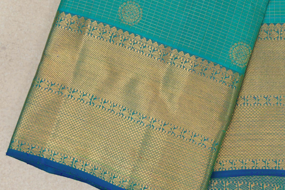 Close-up of folded aqua green Kanjivaram silk saree with fine zari checks, a broad gold-patterned border and a narrow blue edge.