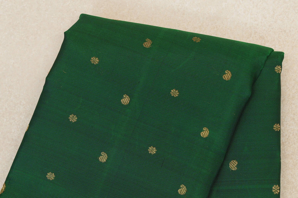 Folded close-up of a bottle green Kanjivaram silk saree body with scattered small gold zari motifs.