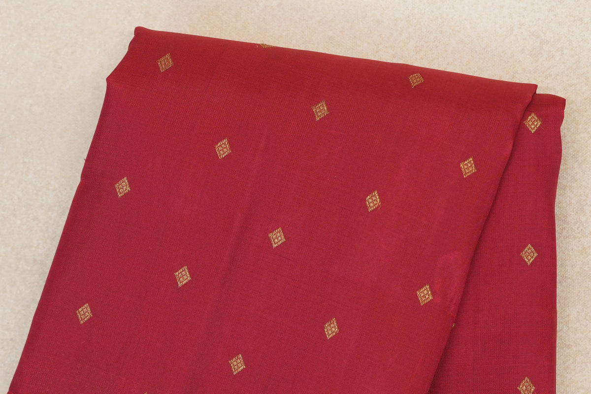 Folded crimson red Kanjivaram silk saree body with small, evenly spaced gold diamond motifs.