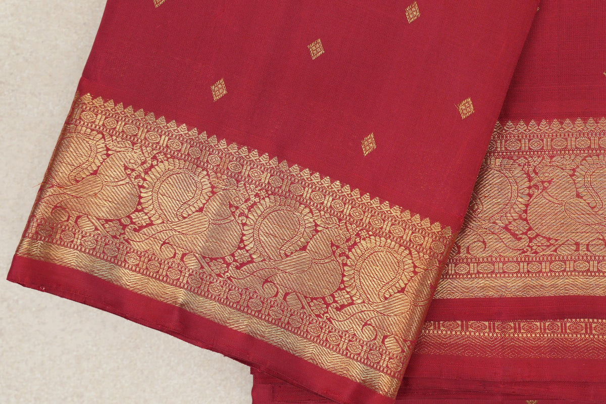 Folded crimson red Kanjivaram silk saree with small gold diamond motifs and a wide gold zari border of large paisley patterns.