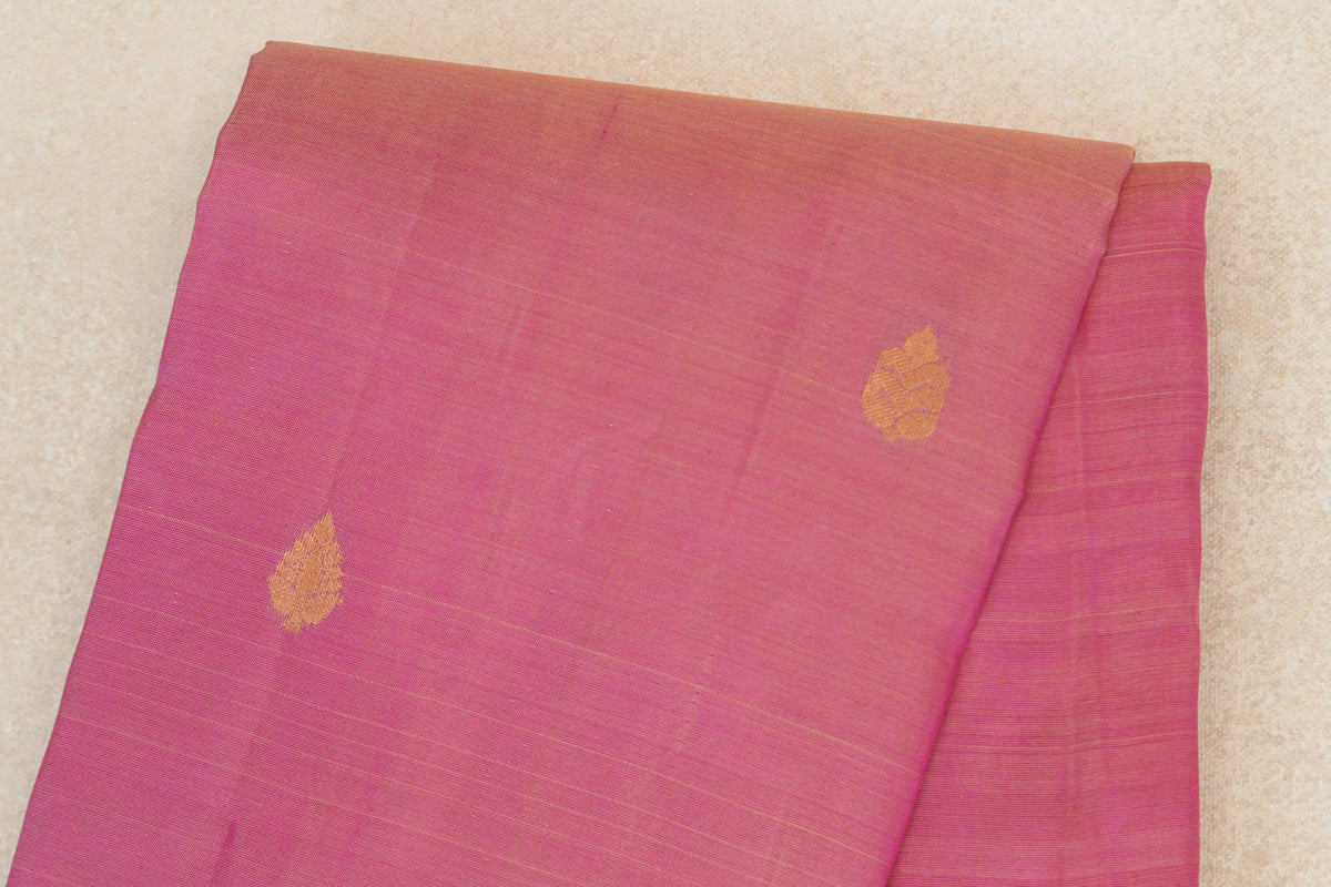 Folded close-up of a rose pink lightweight Kanchipuram silk saree, showing two small gold-toned motifs and fine horizontal lines.