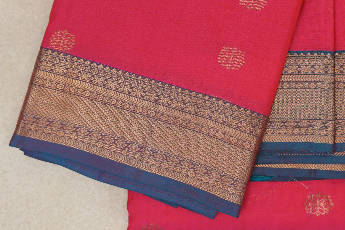 Folded lightweight Kanchipuram silk saree with a bright rani pink body, small gold floral motifs and an ornate teal blue and gold border.