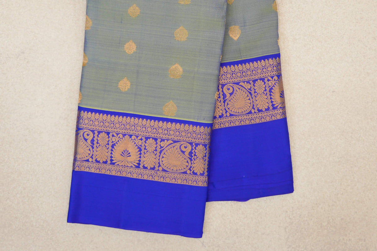 Folded yellowish green lightweight Kanchipuram silk saree with scattered gold motifs and royal blue borders with gold paisley and floral designs.