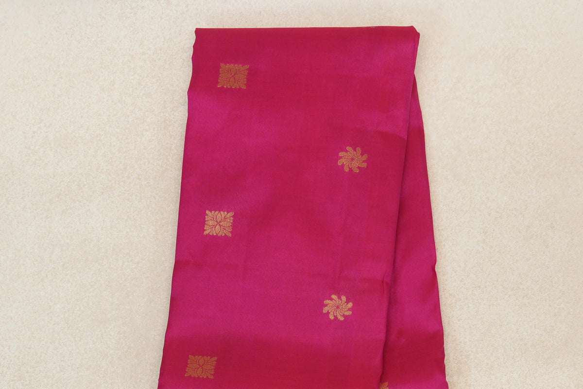 Folded rani pink Kanchipuram silk saree body with spaced gold floral and square motifs.
