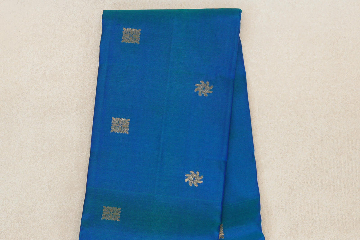 Folded peacock blue lightweight Kanchipuram silk saree with spaced gold floral and square motifs and a deep royal blue edge.