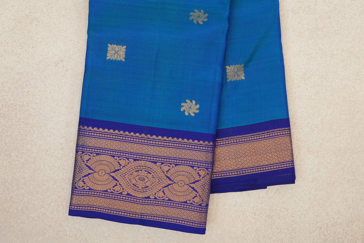 Folded peacock blue Kanchipuram silk saree with scattered gold motifs and a deep royal blue border woven with ornate gold designs.