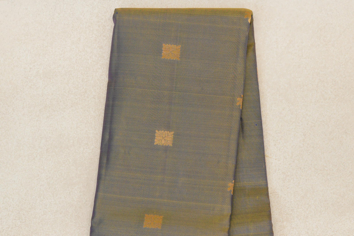 Folded lightweight Kanchipuram silk saree showing a muted violet and yellow body with spaced gold square motifs and a subtly striped edge.