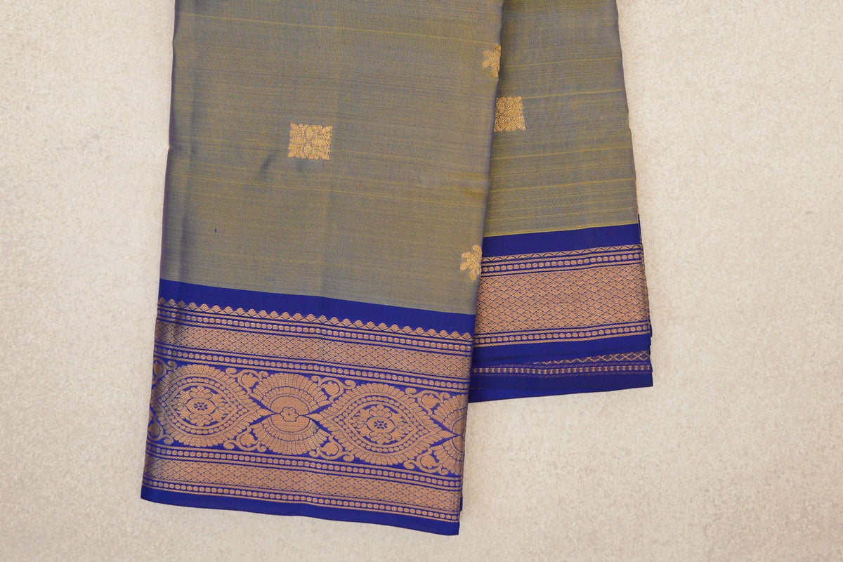 Folded lightweight Kanchipuram silk saree with a yellow and violet body, small gold square motifs and deep royal blue borders with floral and lattice patterns.