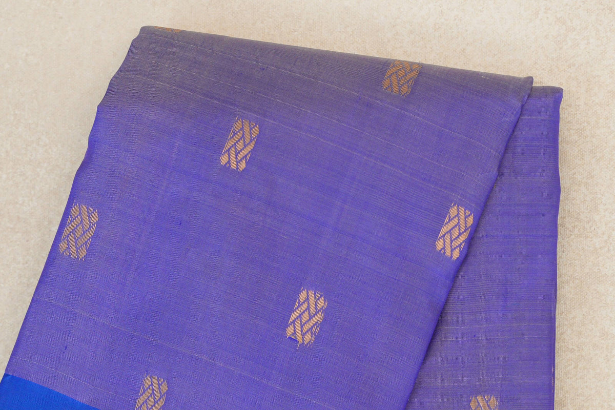 Folded lavender Kanchipuram silk saree with scattered gold geometric motifs and a glimpse of its royal blue border.