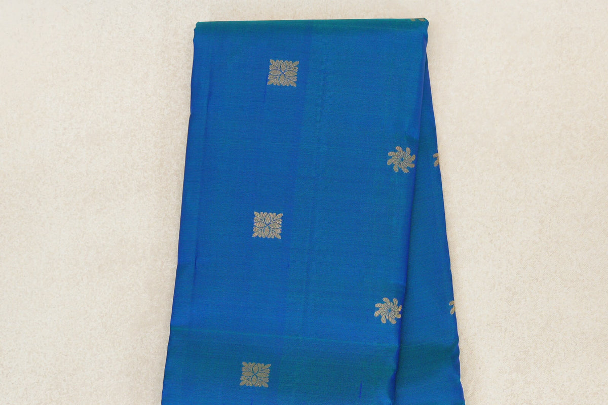 Folded peacock blue lightweight Kanchipuram silk saree showing small, spaced gold-toned floral motifs across the body.