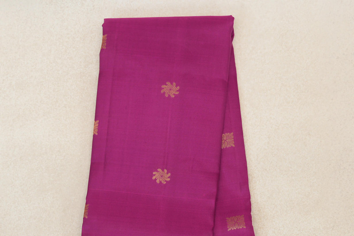 Folded deep magenta Kanchipuram silk saree showing the body with scattered small gold floral motifs.