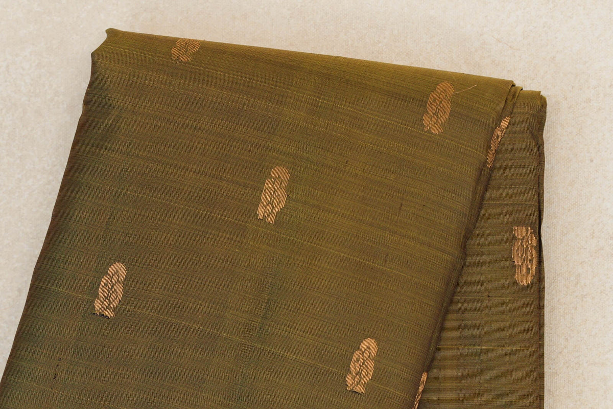Close-up of the folded olive green Kanchipuram silk saree body, with scattered small gold zari motifs and a fine horizontal weave.