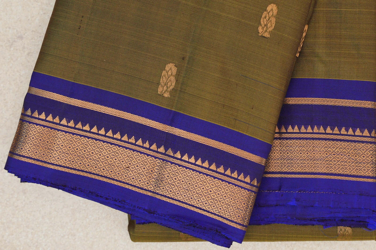 Folded olive green Kanchipuram silk saree with small gold motifs and a deep royal blue border featuring gold geometric bands and temple-style edging.