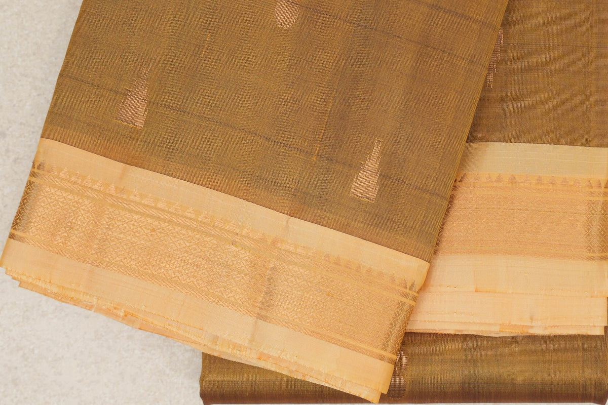 Folded oil mustard Kanchipuram silk saree with small woven accents and wide sandal borders patterned with gold-toned zari.