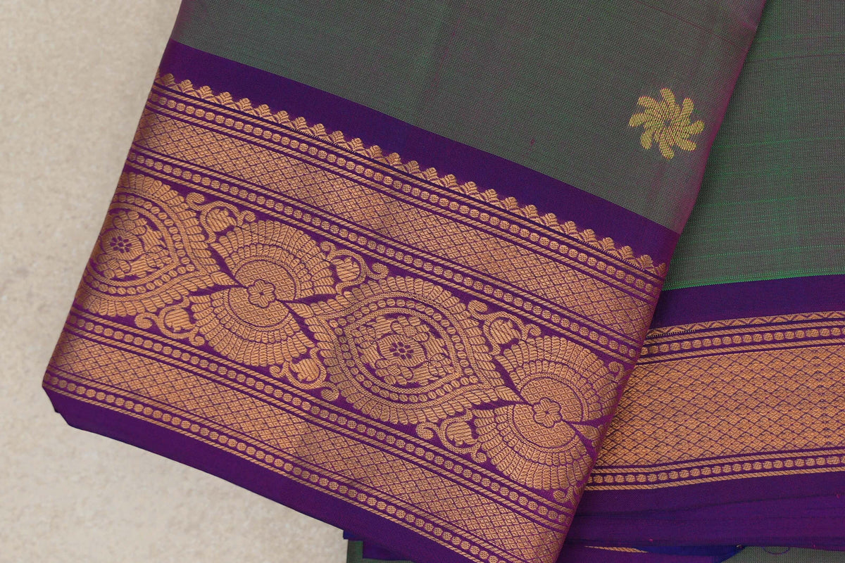 Close-up of a folded lightweight Kanchipuram silk saree, showing a green and pink body with a gold floral motif and an ornate violet purple border.