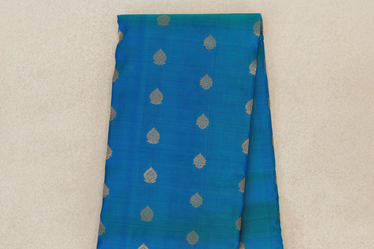 Folded peacock blue Kanchipuram silk saree showing the body with evenly spaced small gold-toned leaf motifs.