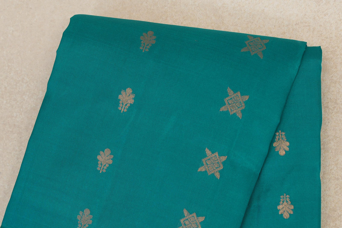 Close-up of a folded peacock green lightweight Kanchipuram silk saree, with scattered gold-toned floral and star-shaped motifs.