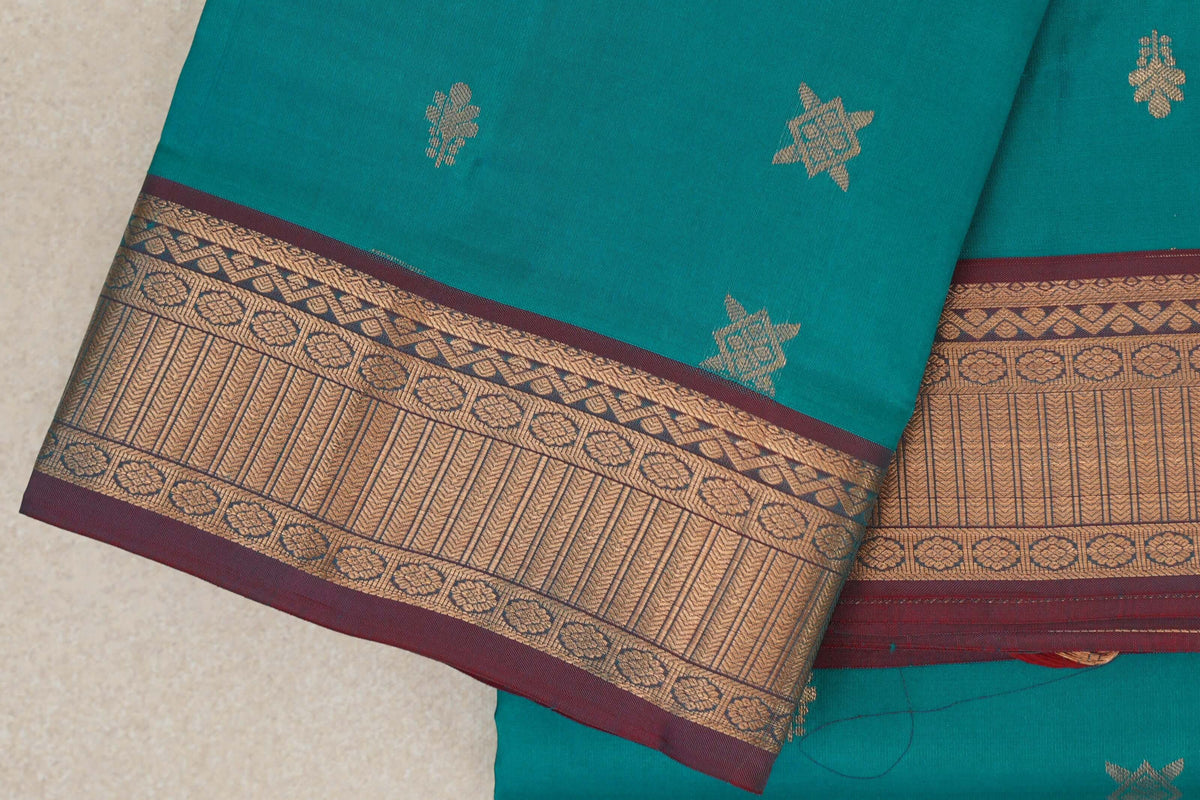 Folded peacock green Kanchipuram silk saree with scattered gold motifs and a broad patterned gold zari border edged in maroon.