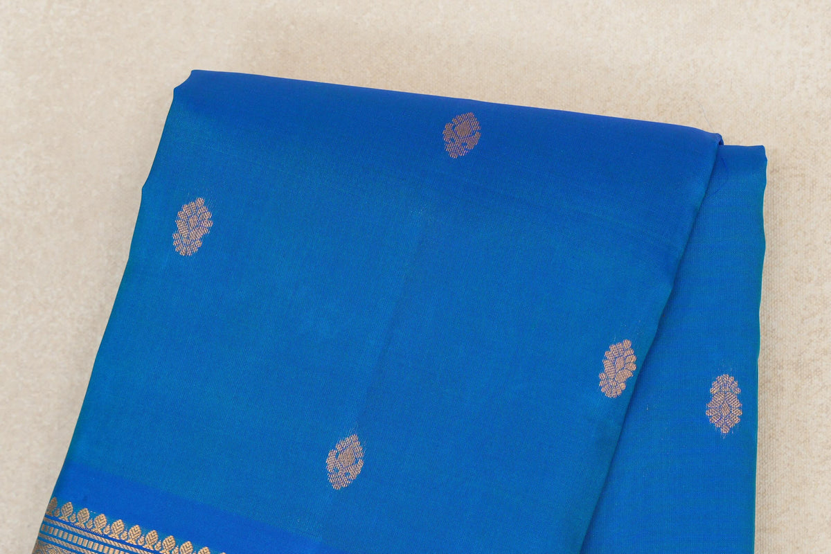 Folded peacock blue lightweight Kanchipuram silk saree with scattered gold-toned motifs and a patterned border visible along one edge.