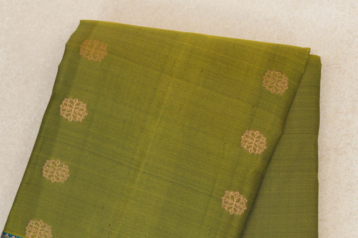 Folded olive green lightweight Kanchipuram silk saree with spaced gold floral motifs and a glimpse of its teal blue border.