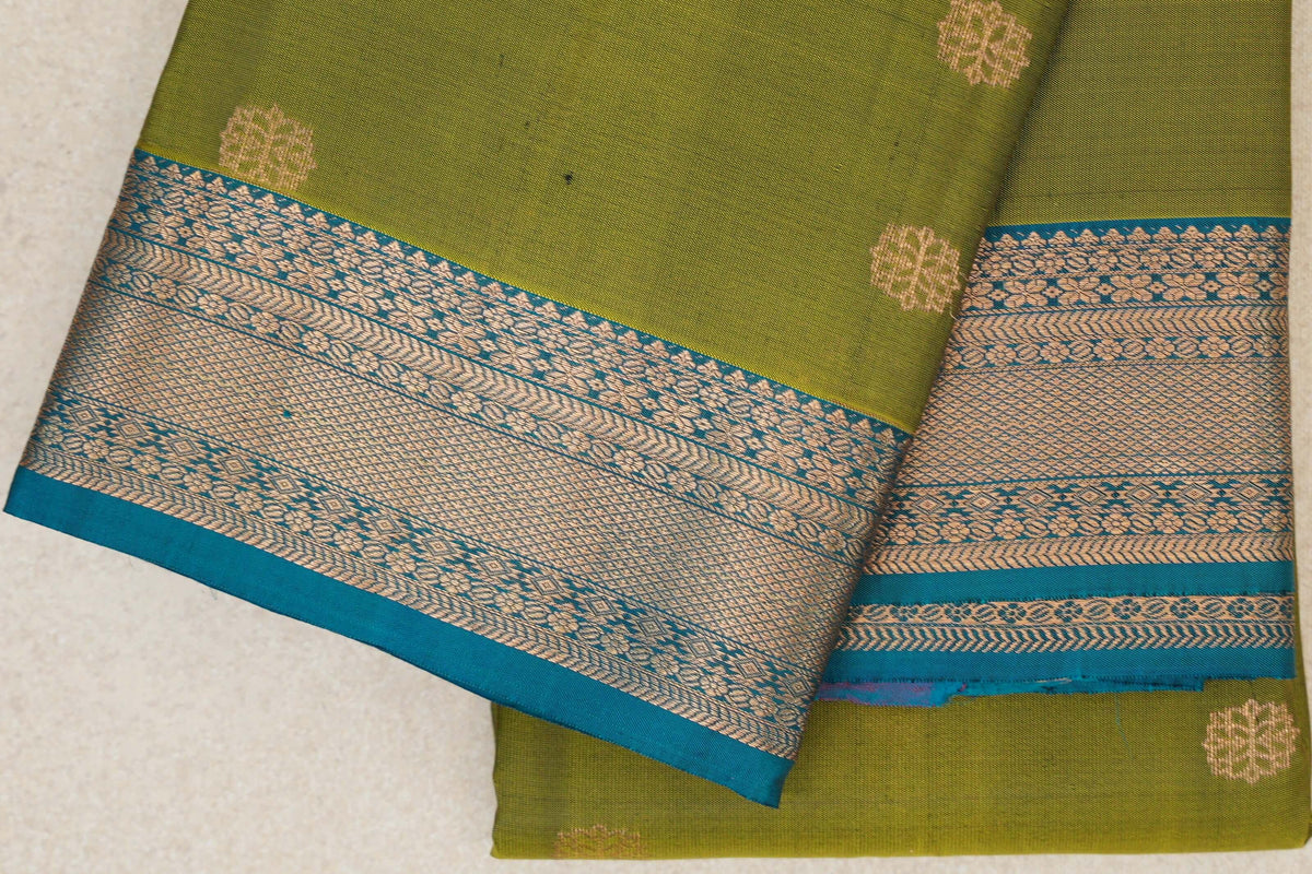 Folded olive green Kanchipuram silk saree with scattered gold floral motifs and a wide teal blue border with intricate gold patterns.