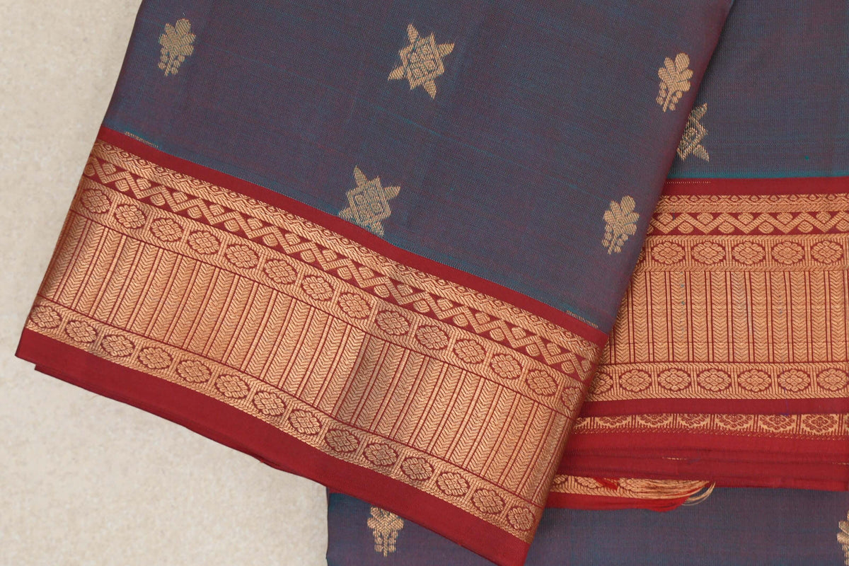 Folded lightweight Kanchipuram silk saree with scattered gold motifs and a deep red border patterned with gold flowers and geometric bands.