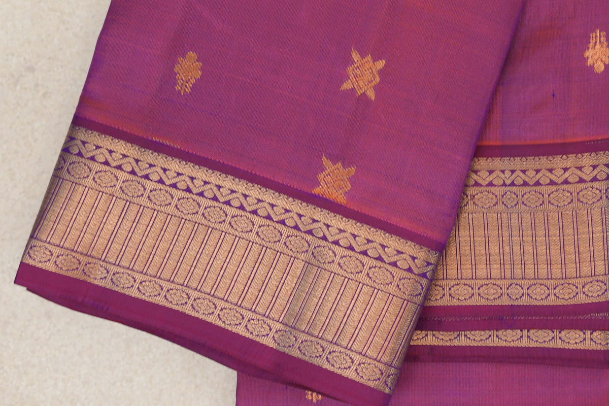 Close-up of a folded blue and red lightweight Kanchipuram silk saree, with scattered gold motifs and a wide patterned gold border.
